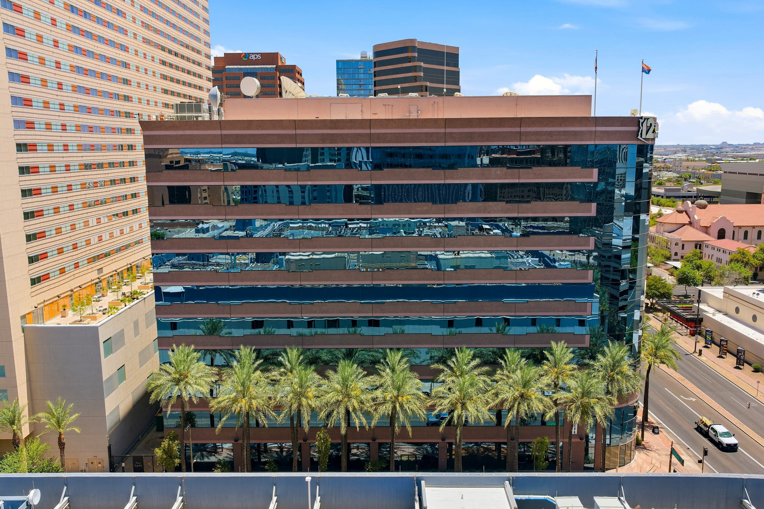 200 East Van Buren seen from the air: a nine-storey building of blue glass and bronze spandrel bands, fronted by a row of palms along Van Buren Street